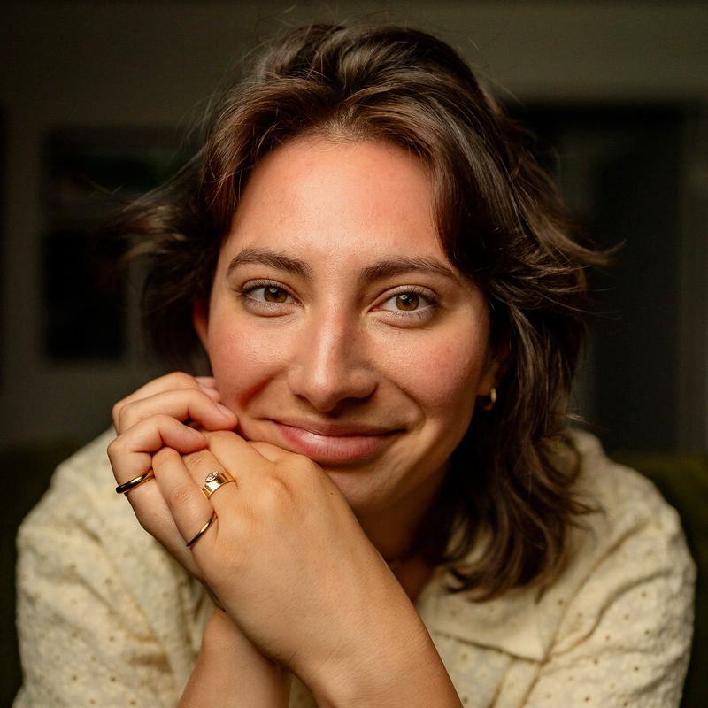 A photo of Isa Medina smiling at the camera. She has brown, short hair, is wearing a cream shirt and rings.